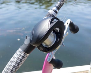 A quartering view of the Bates Goat SWM 200 reel with the surface of a lake behind it.