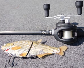 A Bates Goat SWM 200 reel sitting on a carpeted boat deck next to a tattered glide bait.