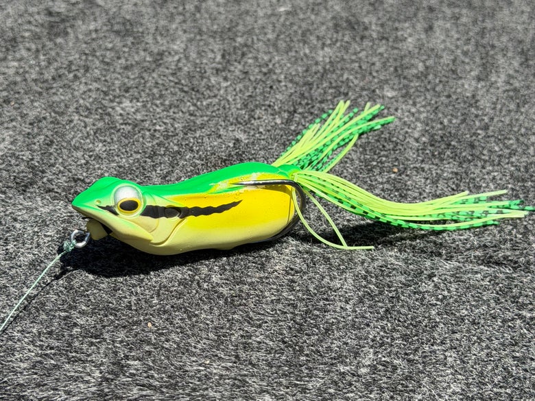 A yellow and green Megabass Big Gabot Frog shown sitting on a carpeted boat deck.