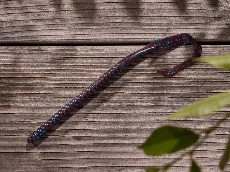 A plum-colored Berkley 12-inch Power Worm sitting on a wood surface.