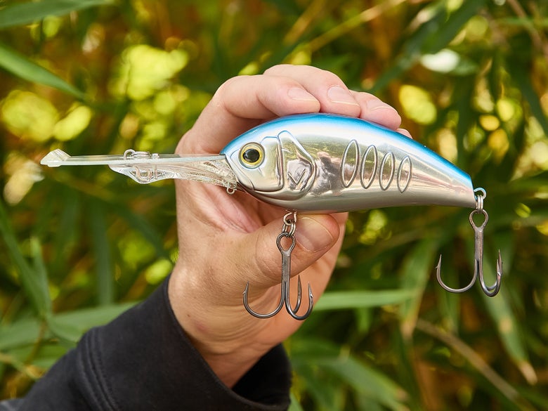 The Deps Korrigan Break 800 crankbait in Blue Shad being held up against a background of foliage.