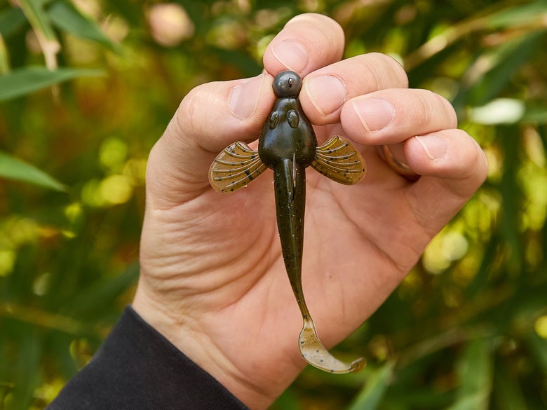 The Jewel Baits Sculpin shown held up while rigged on a ball-head jig head against a foliage background.
