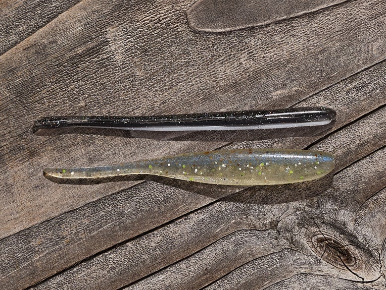 A Keitech Shad Impact and straight-tail finesse Roboworm sitting together on a wood surface.