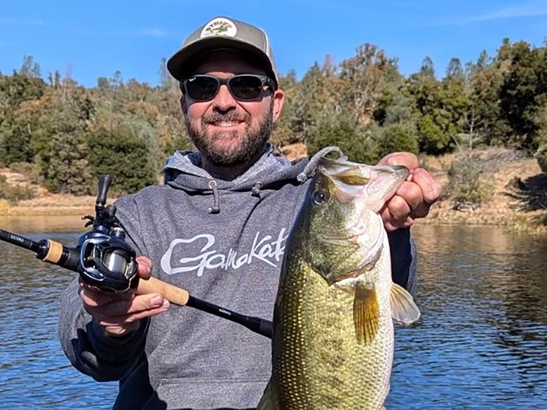 Picture of angler holding a largemouth bas while displaying bfs gear used to catch the fish. 