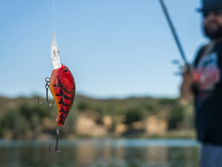 A craw-colored deep-diving crankbait hanging off the end of a rod being held by an angler.