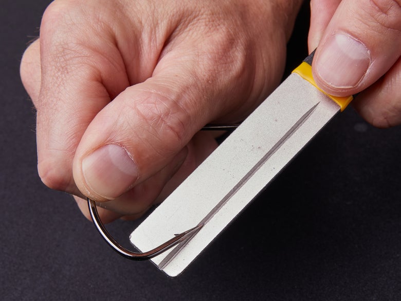 Closeup of a man's hands sharpening a bass hook on a hook file