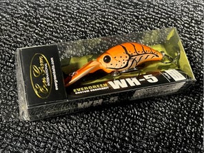 A craw-colored Evergreen Wild Hunch 5 crankbait in its package sitting on a table.